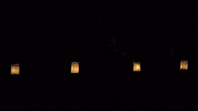 Christmas Eve candle lights flame illuminated in four paper bags at night in row lining street road by residential neighborhood house decoration during holiday on plates