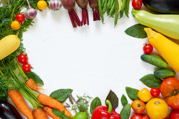 Frame of various vegetarian ingredients ready for cooking on the white table. Organic healthy food: colorful vegetables, herbs and spices on the white background. Top view with copy space for text