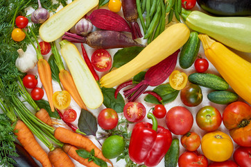 Various fresh organic vegetables on the white table: tomatoes, sliced zucchini, beet, garlic, cabbage, carrots, green beans, bell pepper basil. Cooking concept. Healthy vegetarian diet food background