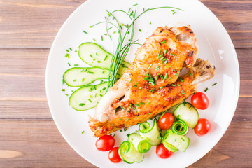 Fototapeta na wymiar Baked turkey wing, cucumber slices and cherry tomatoes on a plate on a wooden table. Top view