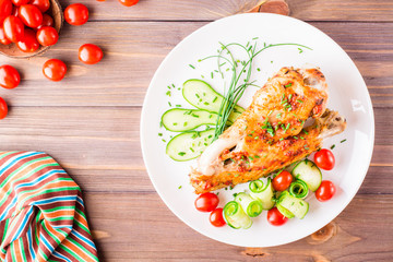 Baked in a spices turkey wing, cucumber slices and cherry tomatoes on a plate on a wooden table. Top view