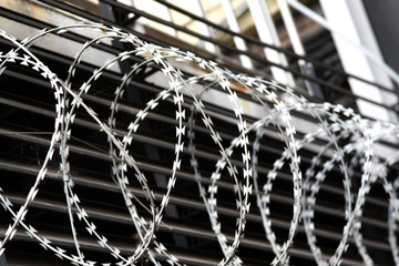 Stacheldraht mit scharfen Widerhaken vor einem hohen Lamellenzaun