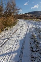 View of Assisi town (Umbria) in winter, with a country road covered by snow and a blue sky with white clouds