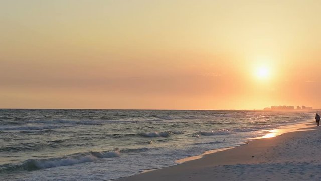 Dreamy pastel orange sunset in Santa Rosa Beach, Florida with Pensacola coastline coast cityscape skyline, man walking, in panhandle with ocean gulf of mexico waves washing, crashing on shore