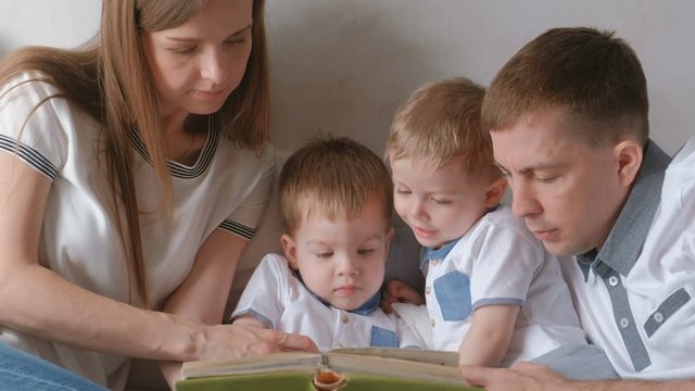 Family mom, dad and two twin brothers read books laying on the bed. Family reading time.