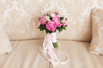 Pink and white wedding bouquet with white tapes on the vintage beige armchair. Closeup