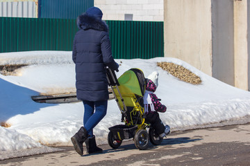 A girl with a stroller walks on the road in winter