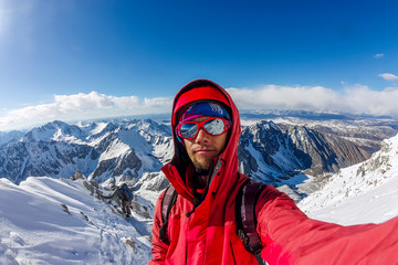 Fototapeta na wymiar Selfi male mountaineer in snowy mountains, wearing a helmet with a backpack