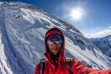 Selfi male mountaineer in snowy mountains, wearing a helmet with a backpack