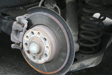 Passenger car with the removal of the wheels is on a hydraulic jack with a naked braking system. Old worn rusty car brake disc with outdated technology. Soft focus, shallow depth of field