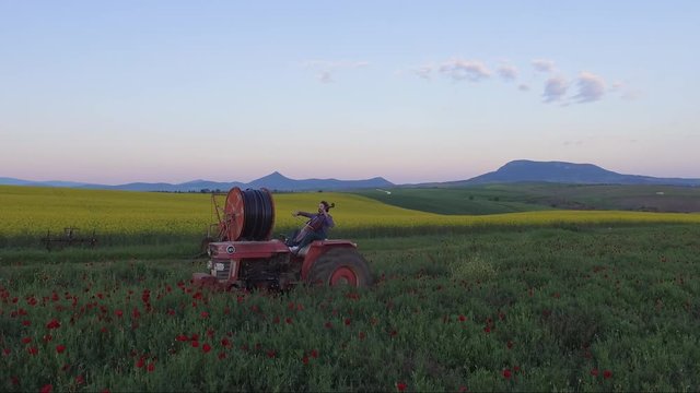 A musician is playing violoncello while driving a tractor in the fields of northern Greece.
