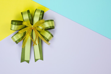 Decorative green ribbon bow on sweet pastel colored paper background texture, view from above with copy space for add text, template for festival or promotion and special day concept.