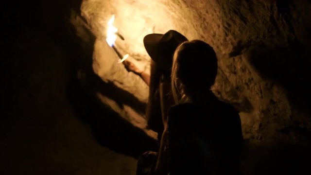 two women exploring a cave or tomb with fire as light
