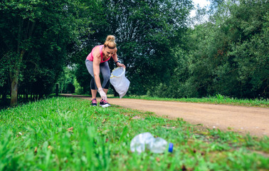 Girl crouching with bag picking up trash doing plogging