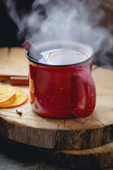 Mulled wine in a red ceramic mug over rustic wooden boards surrounded spices.