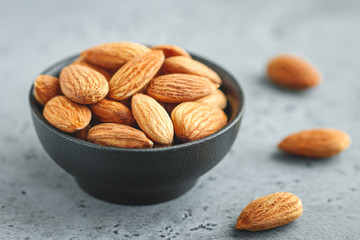 Fresh almond nuts in a back bowl on a textured grey table.
