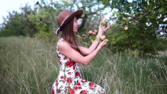 Beautiful blonde girl in hat and dress stands on the apple garden.
