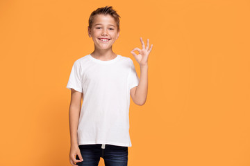 Young emotional little boy on orange studio background.