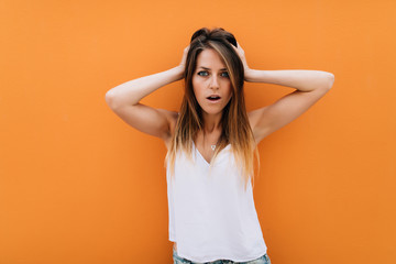 Portrait of beautiful woman with hands on head isolated on orange background