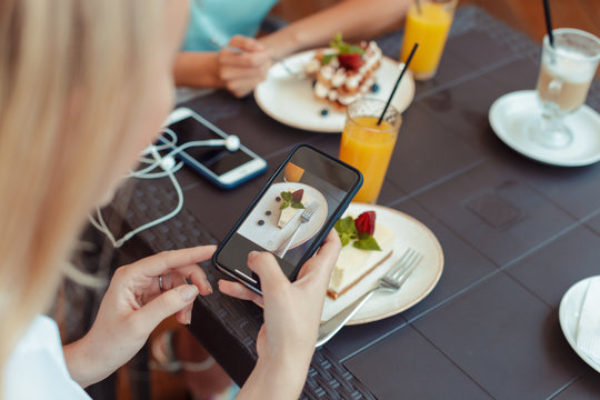 women's hands making photo of sweet dessert on mobile phone while sitting in comfortable restaurant