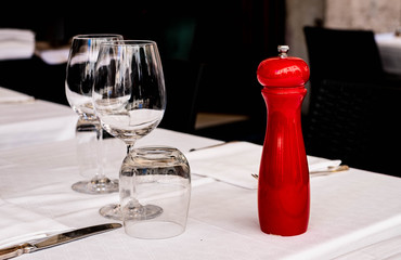Served restaurant table with white tablecloth, empty glasses and red pepper mills on a blurred background