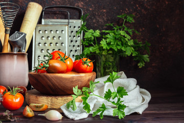 Fresh tomatoes and parsley, dill, garlic on a dark background in a rustic kitchen and wooden utensils still life with copy space