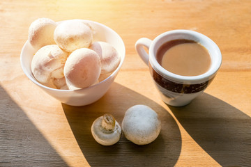 Mushroom Coffee Superfood Trend. Cup of coffee and white bowl with mushrooms on wooden background with sunlight. Caffeine latte, drink, hipster, instagram trend. Coffees for best energy and creativity