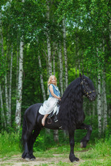 Little girl is riding a friesian horse, outdoor summer
