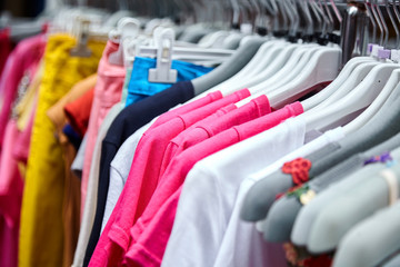Colorful women's summer pants and t-shirts on hangers in a retail shop. Fashion and shopping concept