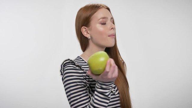 Young sweet ginger girl is biting big apple, enjoying it, offering, communication concept, white background