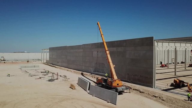 aéreo.colocación de panel de hormigón en el muro de una nave industrial en construcción .grúa y operarios