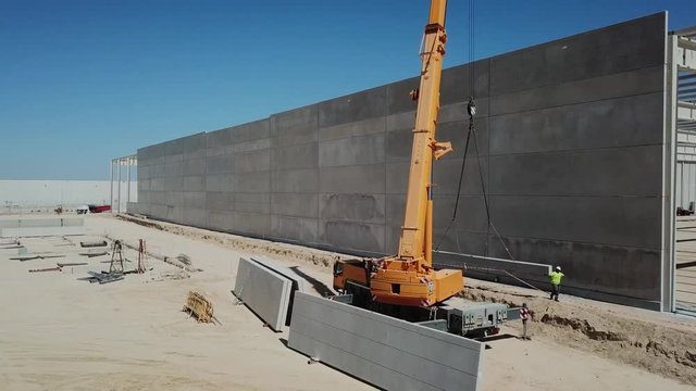 aéreo.colocación de panel de hormigón en el muro de una nave industrial en construcción .grúa y operarios
