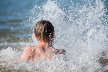 A boy teen swims in a spray of water - a concept of a beach holiday