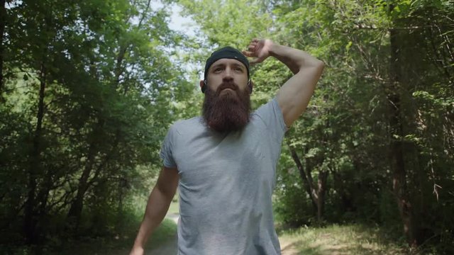 A bearded hipster man runs through the forest with headphones: he listens to music and is focused on running. Jogging in the forest. A lone man runs forward through the forest.
