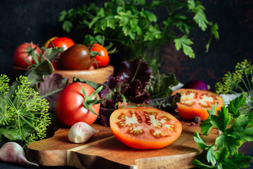 Fresh tomatoes and parsley, dill, garlic on a dark background in a rustic kitchen and wooden utensils still life with copy space