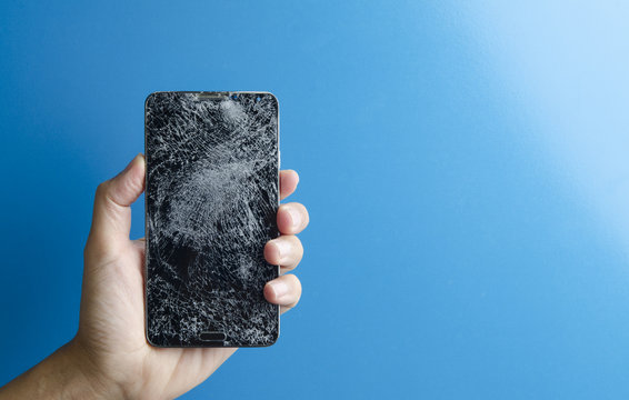 Hand holding broken screen smart phone with blue background