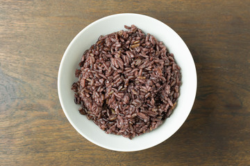 A Cooked rice berry ,Whole grain rice Thai black jasmine rice in bowl  on wood table.