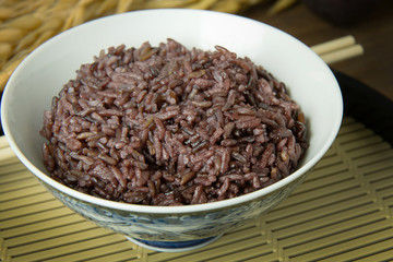 A Cooked rice berry ,Whole grain rice Thai black jasmine rice in bowl  on wood table.