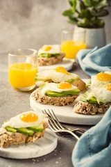 Healthy sandwich with fresh avocado and fried quail egg on small marble board on gray background. Breakfast or lunch food concept with copy space. Retro style toned.