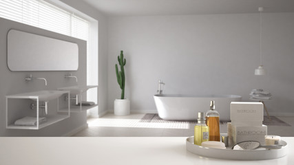 Spa, hotel bathroom concept. White table top or shelf with bathing accessories, toiletries, over blurred minimalist bathroom, modern architecture interior design