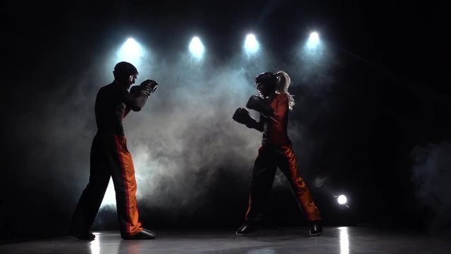 Woman is kicking a guy with their sparring kickboxing. Smoke background. Silhouette. Slow motion