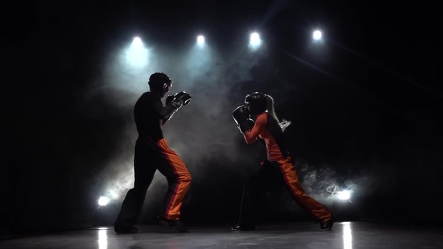 Woman kicking the guy they are sparring for kickboxing . Smoke background. Slow motion. Light from behind