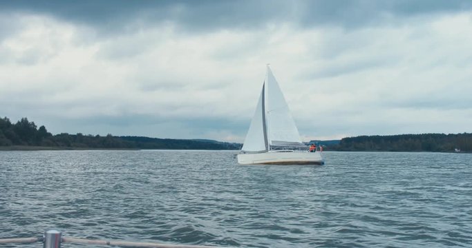 Side view of yacht sailing on a large lake, cloudy weather. 4K UHD 60 FPS SLO MO