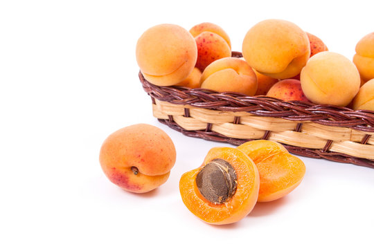 Several of harvested apricots in basket with whole and halved apricots on white background..