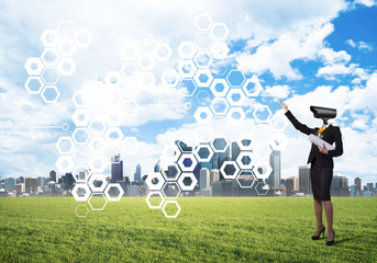 Camera headed woman standing on green grass against modern cityscape