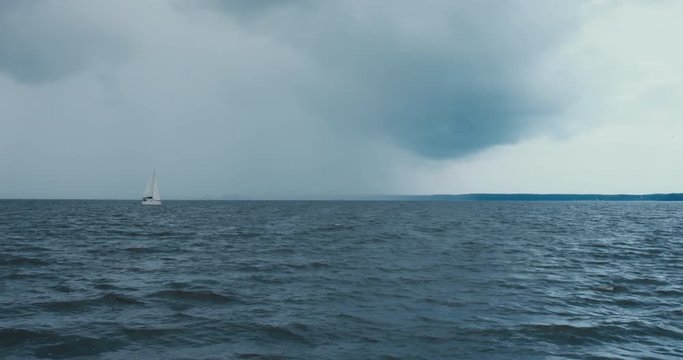 Side view of yacht sailing on a large lake, rainstorm in the background, bad rainy weather. 4K UHD 60 FPS SLO MO