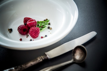 Red raspberry dessert / Fresh ripe fruit served on a white plate with cutlery on dark background. ...