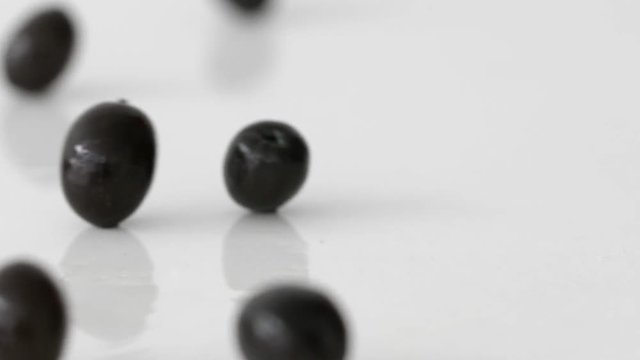 Black olives rolling on a mirror-white surface in slow motion
