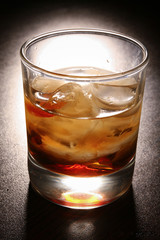 layered alcoholic cocktail with whiskey in a glass glass with ice on a black table