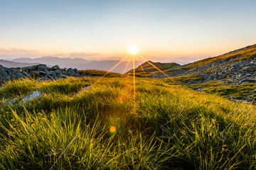 Naklejka premium Sonnenuntergang am Berg mit Gras im Vordergrund